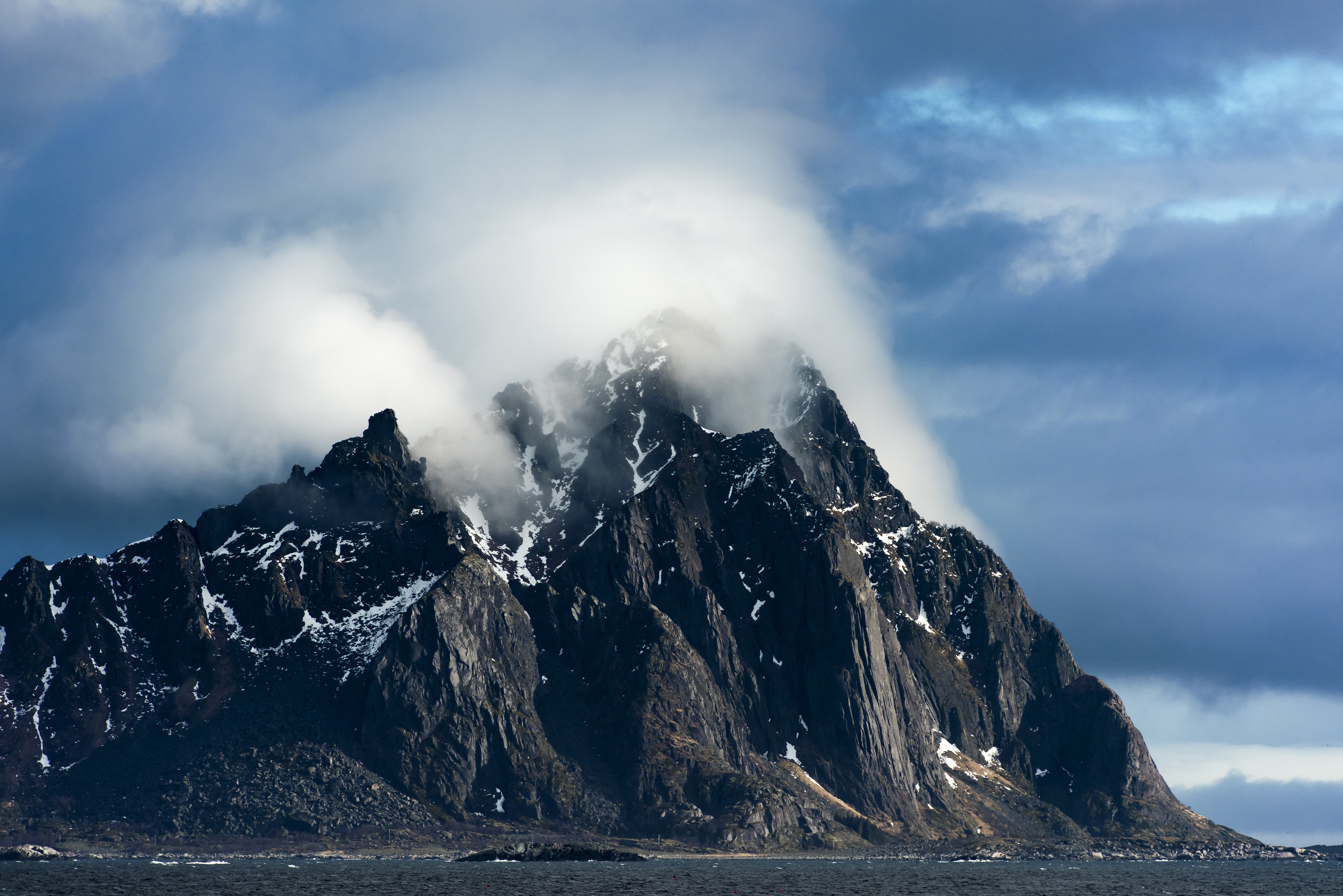 Fjelltopper med skyer ved hav