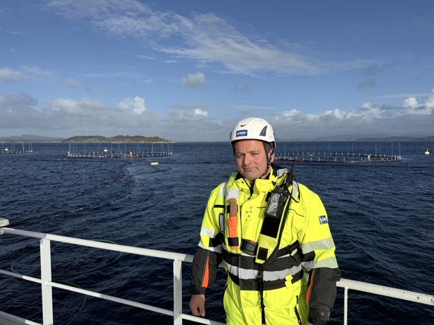 A man in bright yellow work-wear, behind him we see the ocean and skies. 