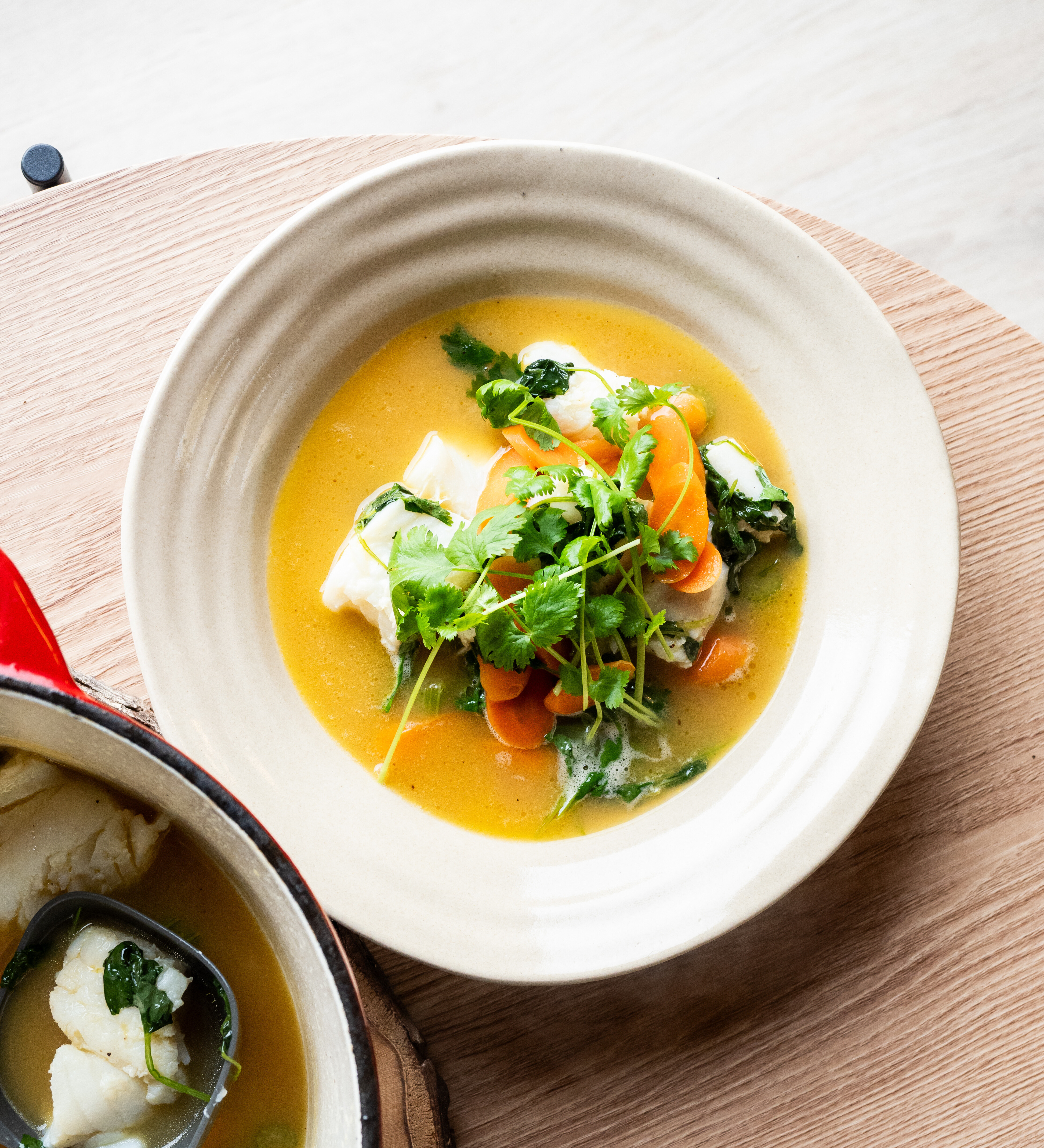 En skål på et bord med fiskesuppe med skrei, gulrot og appelsinkraft